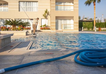 Pool Service Man cleaning a pool with pool vacuum hose coiled on pool deck